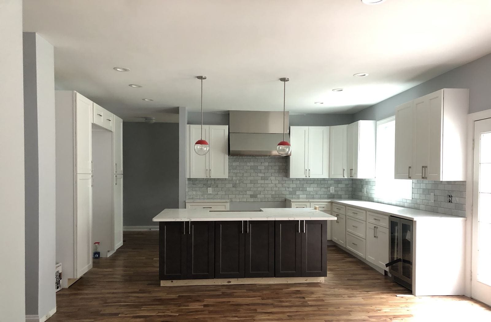 Kitchen addition with a dark island, white cabinets, red pendants and French doors