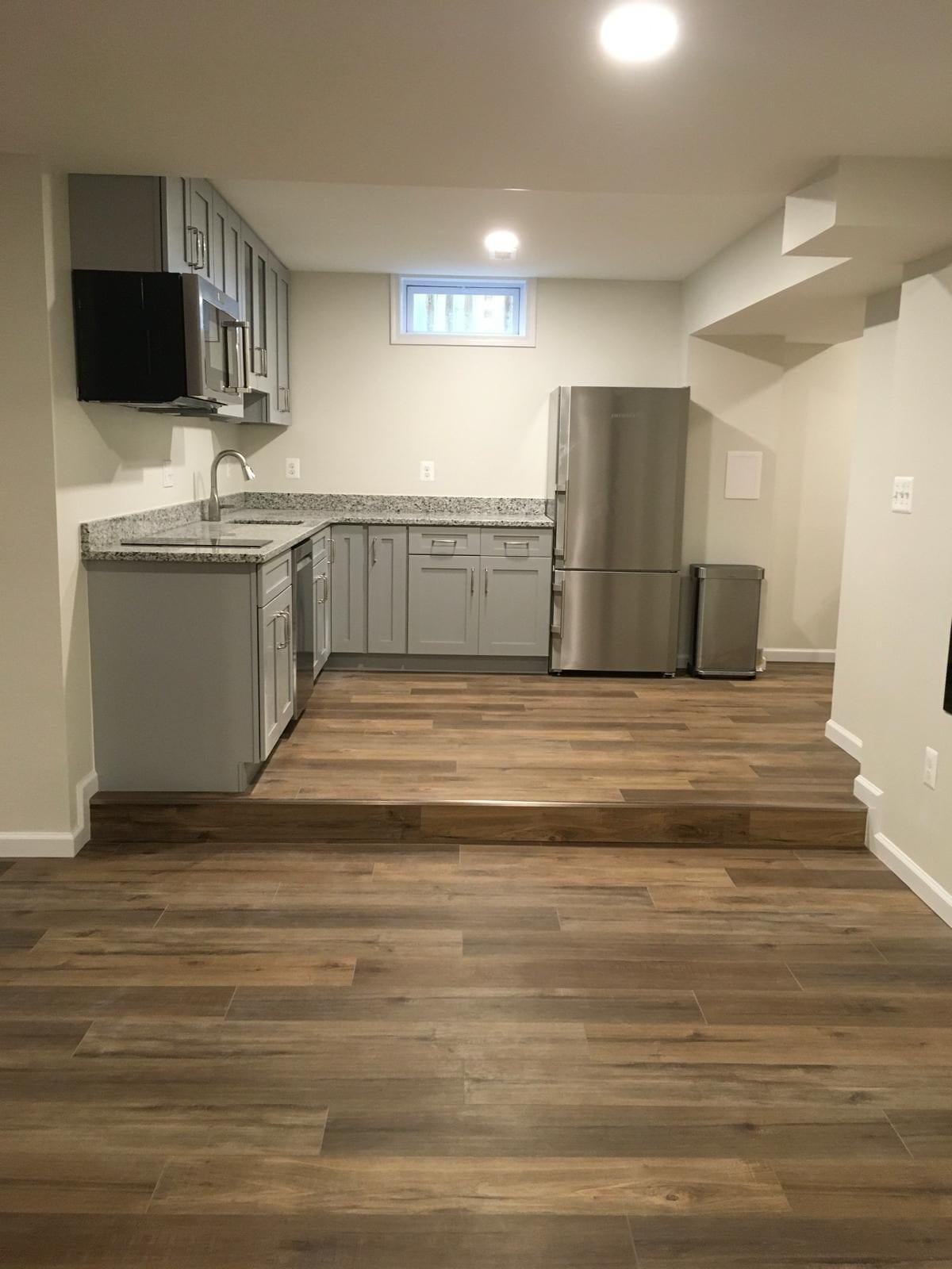 Basement kitchenette in Burke on a raised platform with gray cabinets and a stainless refrigerator