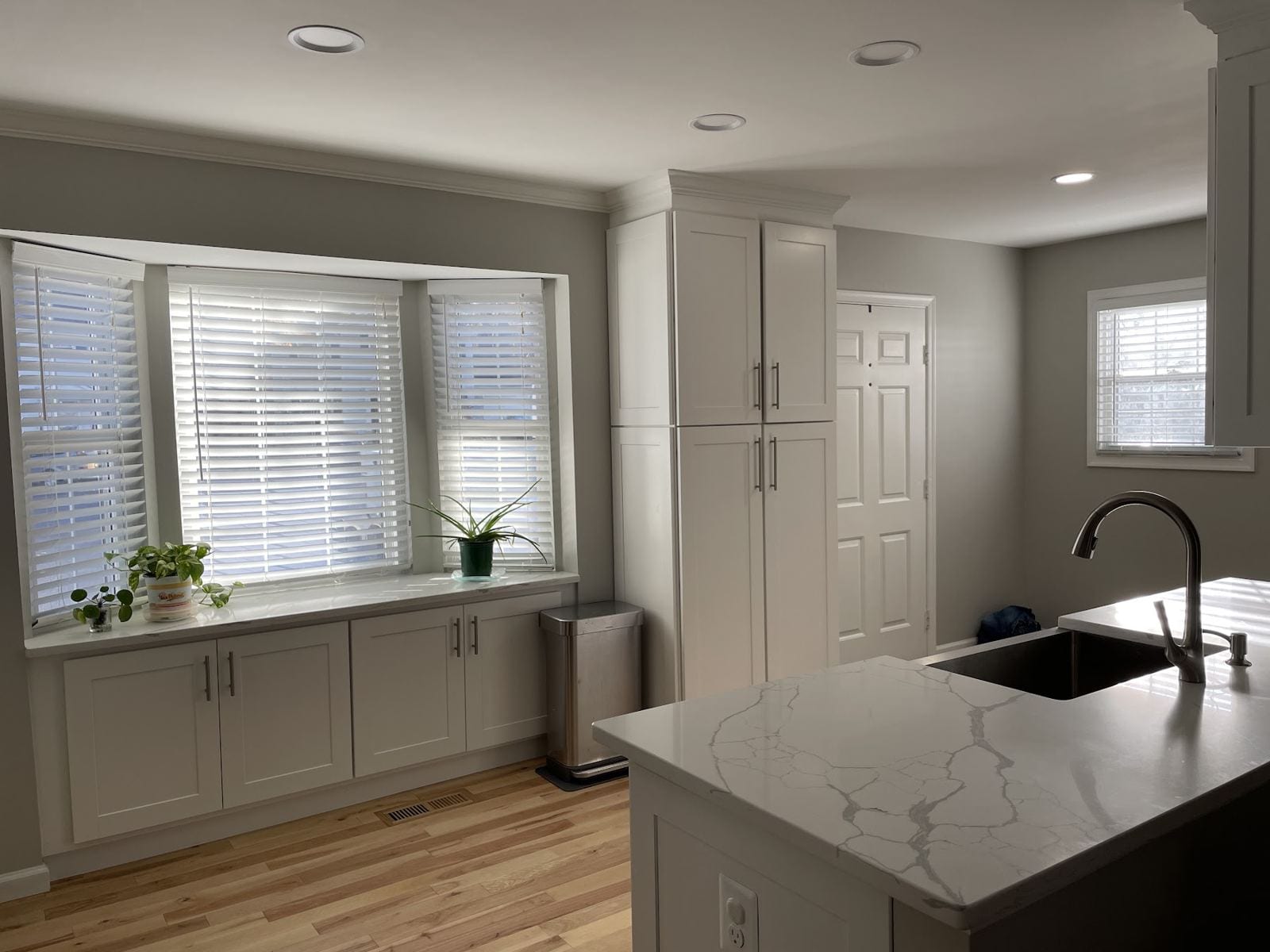Kitchen with a veined quartz peninsula, bay window and tall pantry cabinets